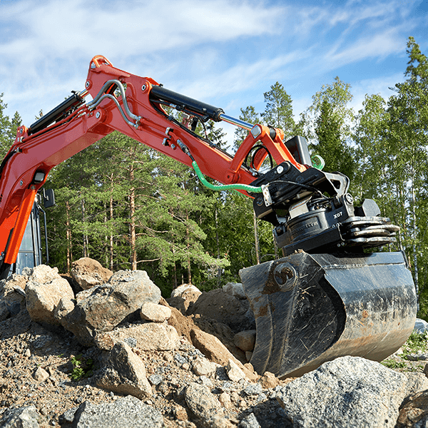 Tiltrator Steelwrist X07 z łyżką roboczą zamontowany na ramieniu koparki podczas pracy w terenie kamienistym