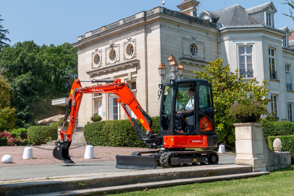 Kubota KX037-4 – widok z boku podczas przejazdu przy budynku